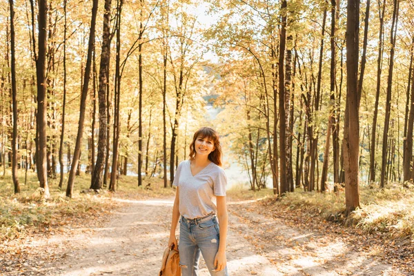 Retrato de jovem mulher no parque de outono. Árvores com folhagem amarela no fundo, bela luz do sol. Camisola quente nos ombros — Fotografia de Stock