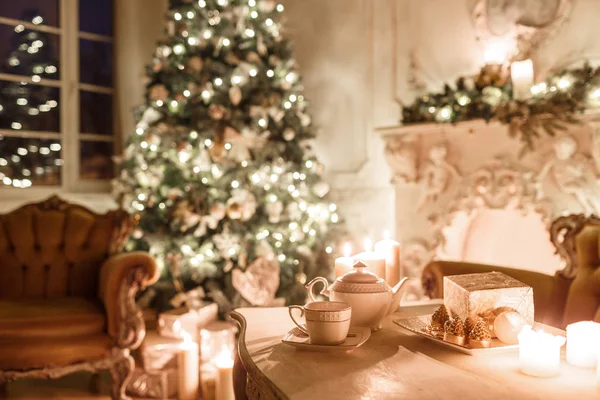 Árbol de Navidad, guirnaldas, velas, linternas, regalos por la noche. interior clásico de una habitación blanca con chimenea decorada, sofá , — Foto de Stock