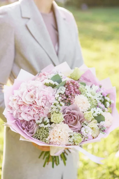 Молода дівчина тримає гарний весняний букет. квіткова композиція з гортензією і садовими трояндами. Колір світло-рожевий. Яскравий світанок або захід сонця — стокове фото