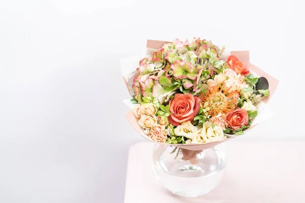 Bellissimo bouquet primaverile. disposizione fiori con vari colori in vaso di vetro su tavolo rosa. stanza luminosa, parete bianca. copia spazio — Foto Stock