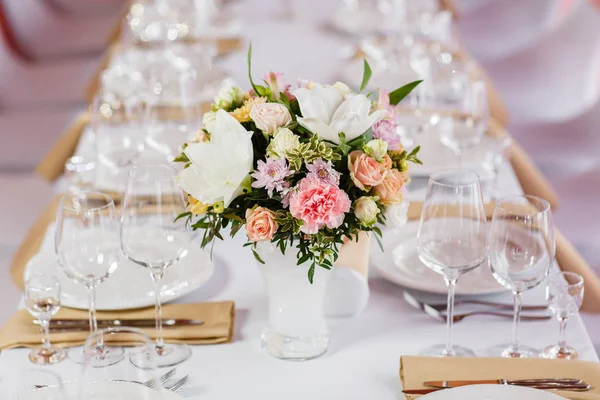 Table at a luxury wedding reception. Beautiful flowers on the table. Serving dishes, glass glasses, waiters work,