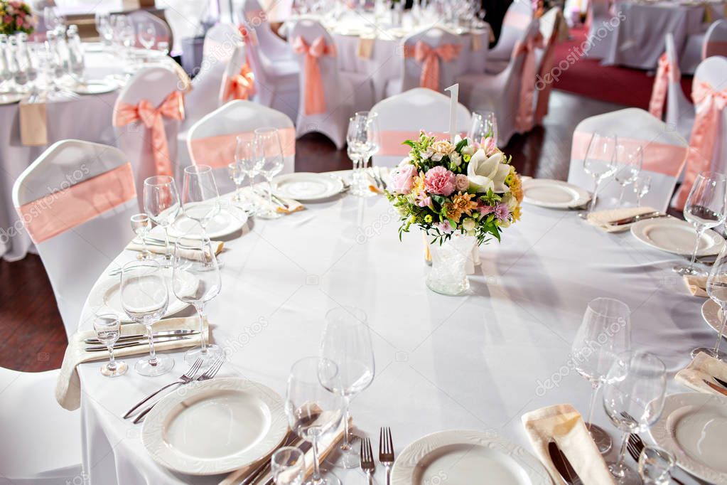 Round table at a luxury wedding reception. Beautiful flowers on the table. Serving dishes, glass glasses, waiters work,