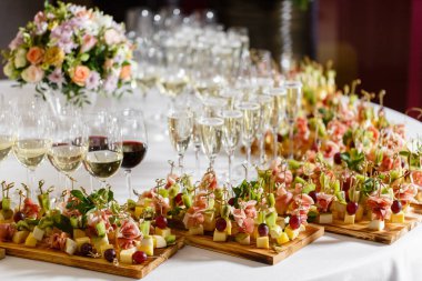 Resepsiyon büfedeki. Bardak şarap ve şampanya. Kanepeler ahşap tahta üzerinde ürün yelpazesine. Ziyafet Servisi. Gıda catering, peynir, jamon, prosciutto ve meyve ile aperatifler