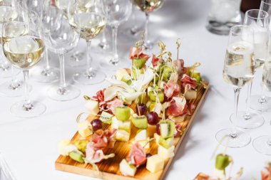 Resepsiyon büfedeki. Bardak şarap ve şampanya. Kanepeler ahşap tahta üzerinde ürün yelpazesine. Ziyafet Servisi. Gıda catering, peynir, jamon, prosciutto ve meyve ile aperatifler