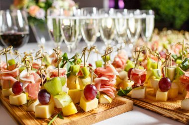 Resepsiyon büfedeki. Bardak şarap ve şampanya. Kanepeler ahşap tahta üzerinde ürün yelpazesine. Ziyafet Servisi. Gıda catering, peynir, jamon, prosciutto ve meyve ile aperatifler