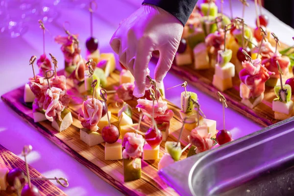 Garson hazırlanan ve bir aperatif hizmet vermektedir. Resepsiyon büfedeki. Kanepeler ahşap tahta üzerinde ürün yelpazesine. Ziyafet Servisi. Gıda catering, peynir, jamon, prosciutto ve meyve ile aperatifler
