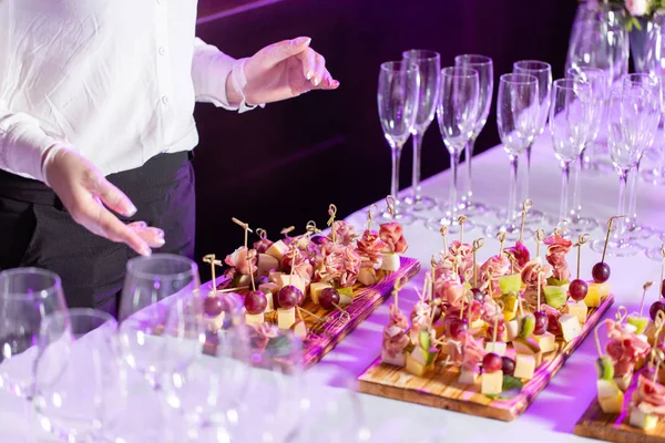 The waiter prepared and serves a snack. the buffet at the reception. Assortment of canapes on wooden board. Banquet service. catering food, snacks with cheese, jamon, prosciutto and fruit — Stock Photo, Image