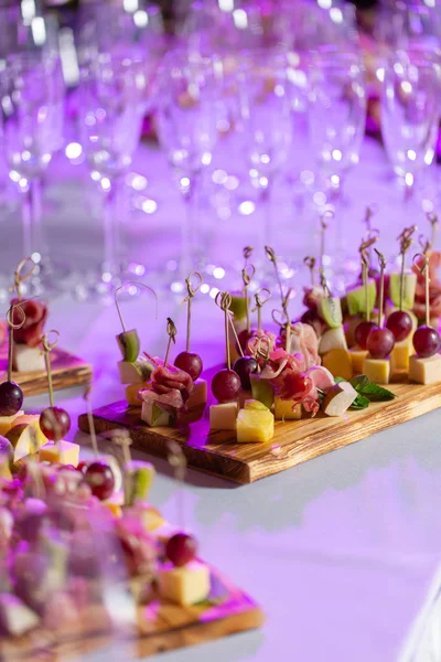 The buffet at the reception. Assortment of canapes on wooden board. Banquet service. catering food, snacks with cheese, jamon, prosciutto and fruit — Stock Photo, Image