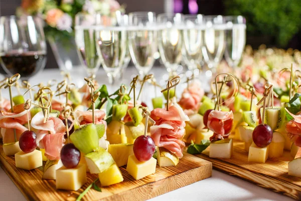 Resepsiyon büfedeki. Bardak şarap ve şampanya. Kanepeler ahşap tahta üzerinde ürün yelpazesine. Ziyafet Servisi. Gıda catering, peynir, jamon, prosciutto ve meyve ile aperatifler