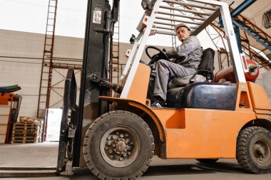 adam bir fabrikada bir ambar yoluyla forklift sürüş. sürücü düzgün ve koruyucu kask içinde. Lojistik ve depolama kavramı