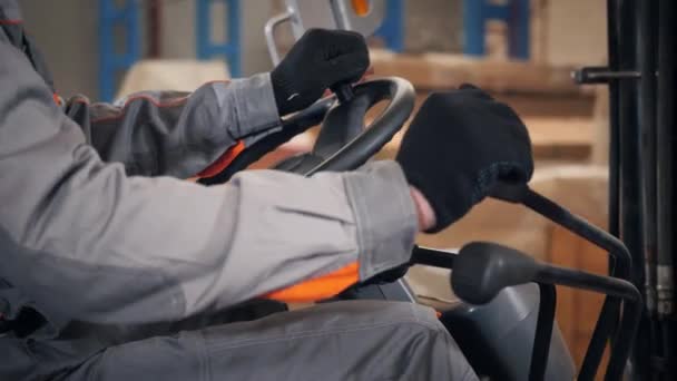 Close-up - stuurwiel en hefbomen. man een heftruck rijden via een magazijn in een fabriek. chauffeur in uniform en beschermende helm. het concept van logistiek en opslag — Stockvideo