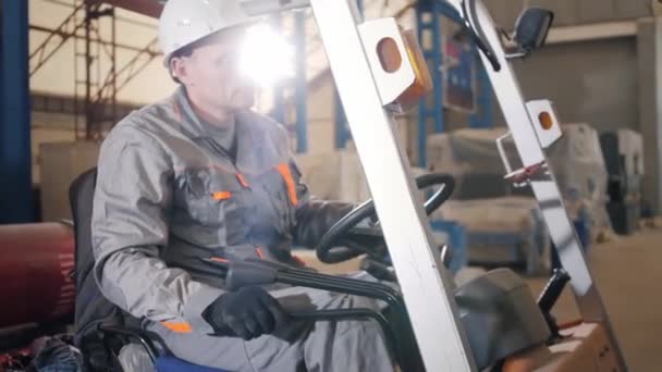 Homem dirigindo uma empilhadeira através de um armazém em uma fábrica. motorista de capacete uniforme e protetor. o conceito de logística e armazenamento — Vídeo de Stock