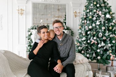 Mutlu bir aile evde eğleniyor. Noel sabahı parlak oturma odasında. Anne ile küçük oğlu. Baba, anne ve bebek oğulları. Yeni Yılınız Kutlu Olsun. süslü Noel ağacı