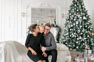 Mutlu bir aile evde eğleniyor. Noel sabahı parlak oturma odasında. Anne ile küçük oğlu. Baba, anne ve bebek oğulları. Yeni Yılınız Kutlu Olsun. süslü Noel ağacı