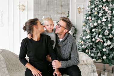 Mutlu bir aile evde eğleniyor. Noel sabahı parlak oturma odasında. Anne ile küçük oğlu. Baba, anne ve bebek oğulları. Yeni Yılınız Kutlu Olsun. süslü Noel ağacı