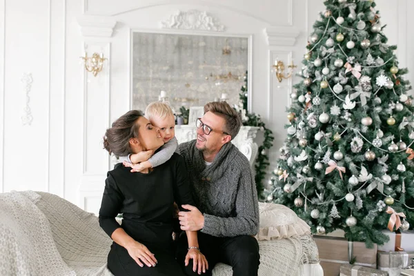 Mutlu bir aile evde eğleniyor. Noel sabahı parlak oturma odasında. Anne ile küçük oğlu. Baba, anne ve bebek oğulları. Yeni Yılınız Kutlu Olsun. süslü Noel ağacı
