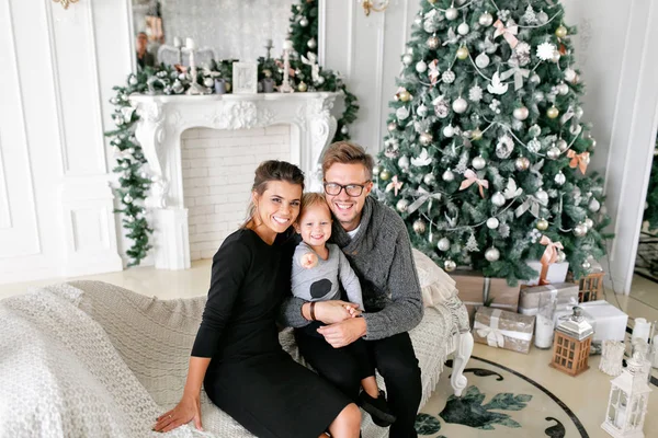 Šťastná rodina baví doma. Vánoční dopoledne v obývací pokoj. Mladí rodiče s malým synem. otec, matka a jejich chlapeček. Šťastný nový rok. zdobené vánoční strom — Stock fotografie