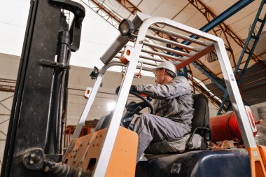 adam bir fabrikada bir ambar yoluyla forklift sürüş. sürücü düzgün ve koruyucu kask içinde. Lojistik ve depolama kavramı