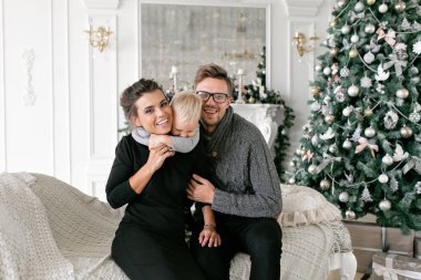 Mutlu bir aile evde eğleniyor. Noel sabahı parlak oturma odasında. Anne ile küçük oğlu. Baba, anne ve bebek oğulları. Yeni Yılınız Kutlu Olsun. süslü Noel ağacı