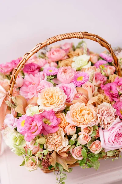 Цветочная композиция с различными цветами в плетеной корзине на розовом столе. красивый весенний букет. светлая комната, белая стена. копировальное пространство — стоковое фото