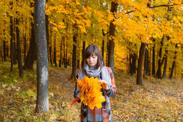 Portrét mladé dívky, které jsou venkovní. Kytice s žluté lístečky v jejích rukou. Bruneta žena v podzimním parku s módní kostkovaný kabát a šátek. — Stock fotografie