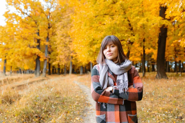 Retrato de mujer joven en bosque otoñal. Mujer morena en el parque de otoño con abrigo a cuadros de moda y bufanda . —  Fotos de Stock