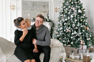 Mutlu bir aile evde eğleniyor. Noel sabahı parlak oturma odasında. Anne ile küçük oğlu. Baba, anne ve bebek oğulları. Yeni Yılınız Kutlu Olsun. süslü Noel ağacı