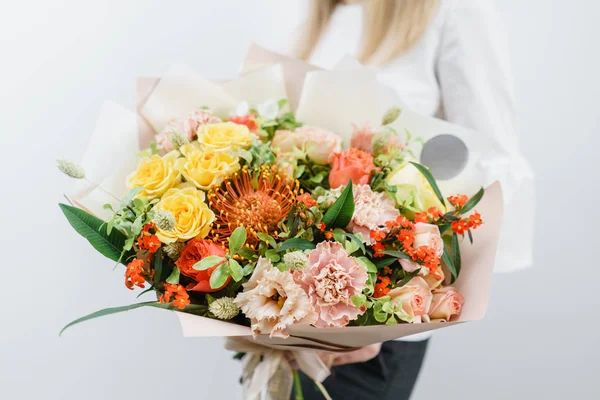 Hermoso ramo de primavera. Chica joven sosteniendo un arreglo de flores con varios colores. pared blanca . — Foto de Stock