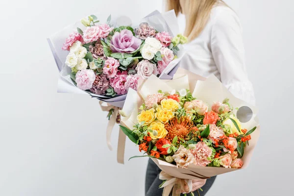 Due bellissimi bouquet primaverili. Giovane ragazza che tiene un composizioni floreali con vari colori. parete bianca . — Foto Stock