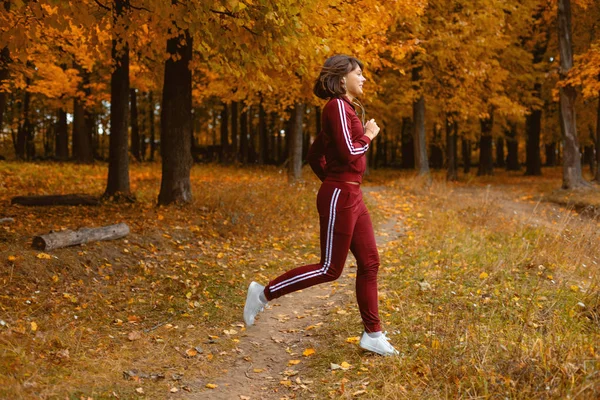 Retrato de uma jovem mulher na floresta de outono. Mulher morena no parque de outono faz uma corrida e aquecer. Estilo de vida desportivo — Fotografia de Stock