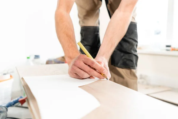 Hombre trabajador aplica marcas a la Junta para el corte con una sierra electrostática. la instalación de nuevos pisos laminados de madera. concepto de reparación en casa . — Foto de Stock