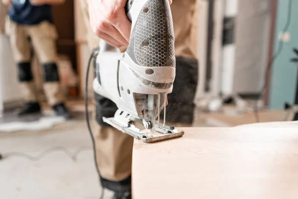Hombre trabajador corta la placa laminada con una sierra electrostática. la instalación de nuevos pisos laminados de madera. concepto de reparación en casa . — Foto de Stock