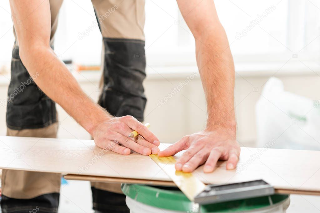 Male worker applies markings to the Board for cutting with a electrofret saw. installing new wooden laminate flooring. concept of repair in house.