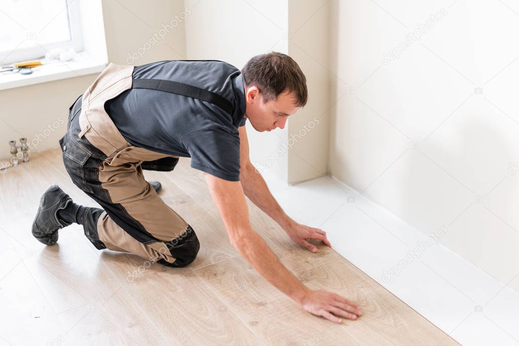 Male worker installing new wooden laminate flooring on a warm film foil floor. infrared floor heating system under laminate floor