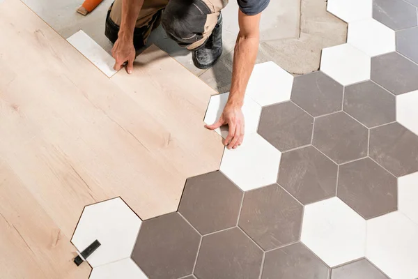 Mužské pracovní instalace nové dřevěné laminátové podlahy. Kombinace dřevěných panelů laminátové a keramických dlaždic v podobě plástve. Rekonstrukce kuchyně. — Stock fotografie