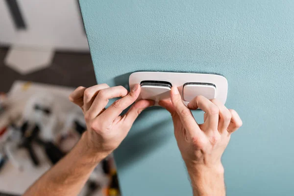 Electrician worker installs light switch and socket on wall in room. Screwdriver, close-up electrician hands.