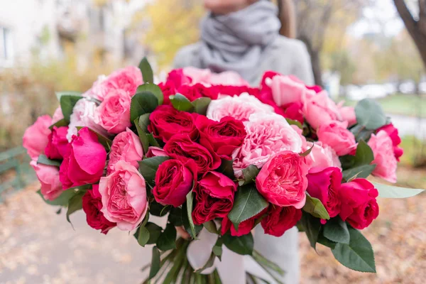 Big luxury bright bouquet in the hands of a cute girl. One hundred garden roses, varieties of David Austin. Three kinds of bright pink, scarlet and pastel colors. Autumn leaves in the Park. — Stock Photo, Image