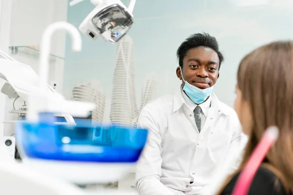 Mladý africký americký lékař zubař v lékařské masku. Krásná dívka pacienta na židli na zubní klinice. Lékařství, zdravotnictví, stomatologie koncept. zubní lékař provádí kontroly a uzavírá — Stock fotografie