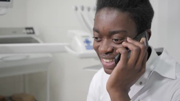 Fiatal afroamerikai férfi orvos fogászat fogorvosi rendelőben. a beteg beszél a telefonon. Orvostudomány, egészség, Sztomatológia koncepció. — Stock videók