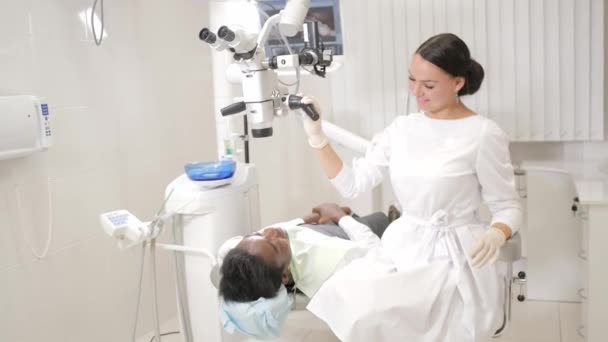 Charmiga vacker flicka läkare tandläkare. Ung African American manlig patient på stolen vid tandvårdsklinik. Medicin, hälsa, Stomatologi koncept. tandläkare genomför inspektion och avslutar. — Stockvideo