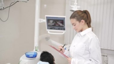 Büyüleyici güzel kız doktor diş hekimi. Genç Afro-Amerikan erkek hasta sandalyeye diş kliniği. Tıp, sağlık, stomatology kavramı. diş hekimi muayene yapar ve bitirmek adl. Gülümseyen kadın