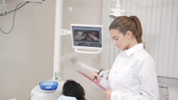 Rozkošný zubař doktor krásnou dívku. Mladý Američan Afričana pacient v křesle na zubní klinice. Lékařství, zdravotnictví, stomatologie koncept. zubní lékař provádí kontroly a uzavírá. Žena s úsměvem — Stock video