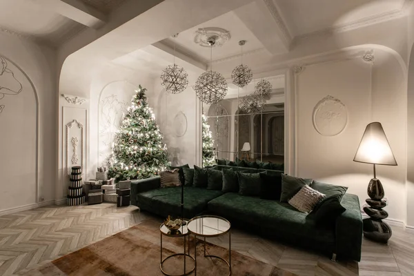 Garland glödlampor. Jul kväll. klassiska lyxiga lägenheter med dekorerad julgran. Vardagsrum hall stor spegel, grön soffa, höga fönster, kolumner och stuckatur. — Stockfoto