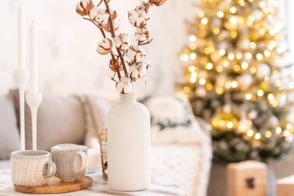 Vase mit Baumwollzweigen vorhanden. helles Wohnzimmer mit Weihnachtsbaum. bequemes Sofa, hohe große Fenster — Stockfoto