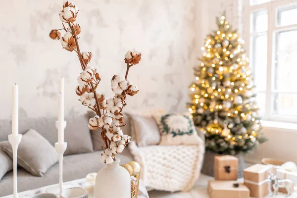 Vase mit Baumwollzweigen vorhanden. helles Wohnzimmer mit Weihnachtsbaum. bequemes Sofa, hohe große Fenster — Stockfoto