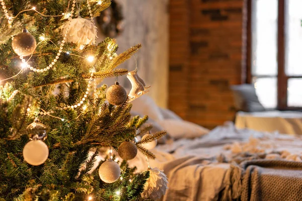 Ramas de abeto decoradas en primer plano. Loft apartamentos, pared de ladrillo con velas y árbol de Navidad. Cama en el dormitorio, grandes ventanales —  Fotos de Stock