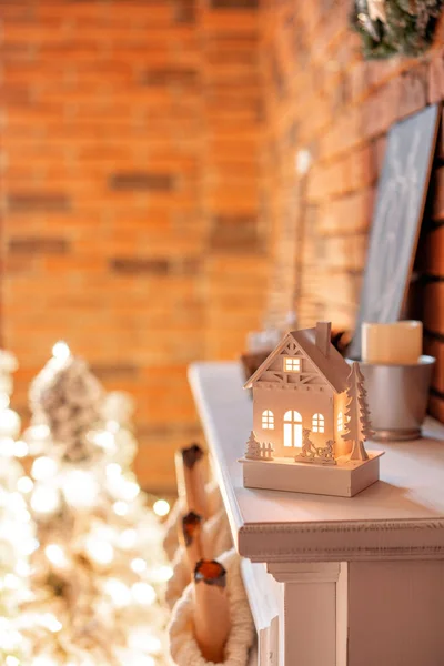 Pequena casa de madeira com uma vela dentro. Meias de lã branca para o Pai Natal na lareira. Apartamentos Loft, parede de tijolo com velas e grinalda árvore de Natal . — Fotografia de Stock