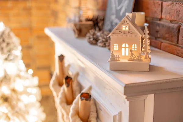 Маленький деревянный дом со свечой внутри. Белые шерстяные носки для Санты на камине. Квартиры в лофте, кирпичная стена со свечами и венком из елки . — стоковое фото