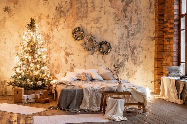 Loft apartamentos, pared de ladrillo con velas y corona de árboles de Navidad. Cama en el dormitorio, grandes ventanales — Foto de Stock