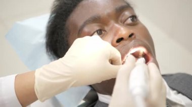 Diş hekimi makro fotoğraf makinesi ağız boşluğu hastanın ile inceliyor. Genç Afro-Amerikan erkek hasta sandalyeye diş kliniği. Tıp, sağlık, stomatology kavramı.